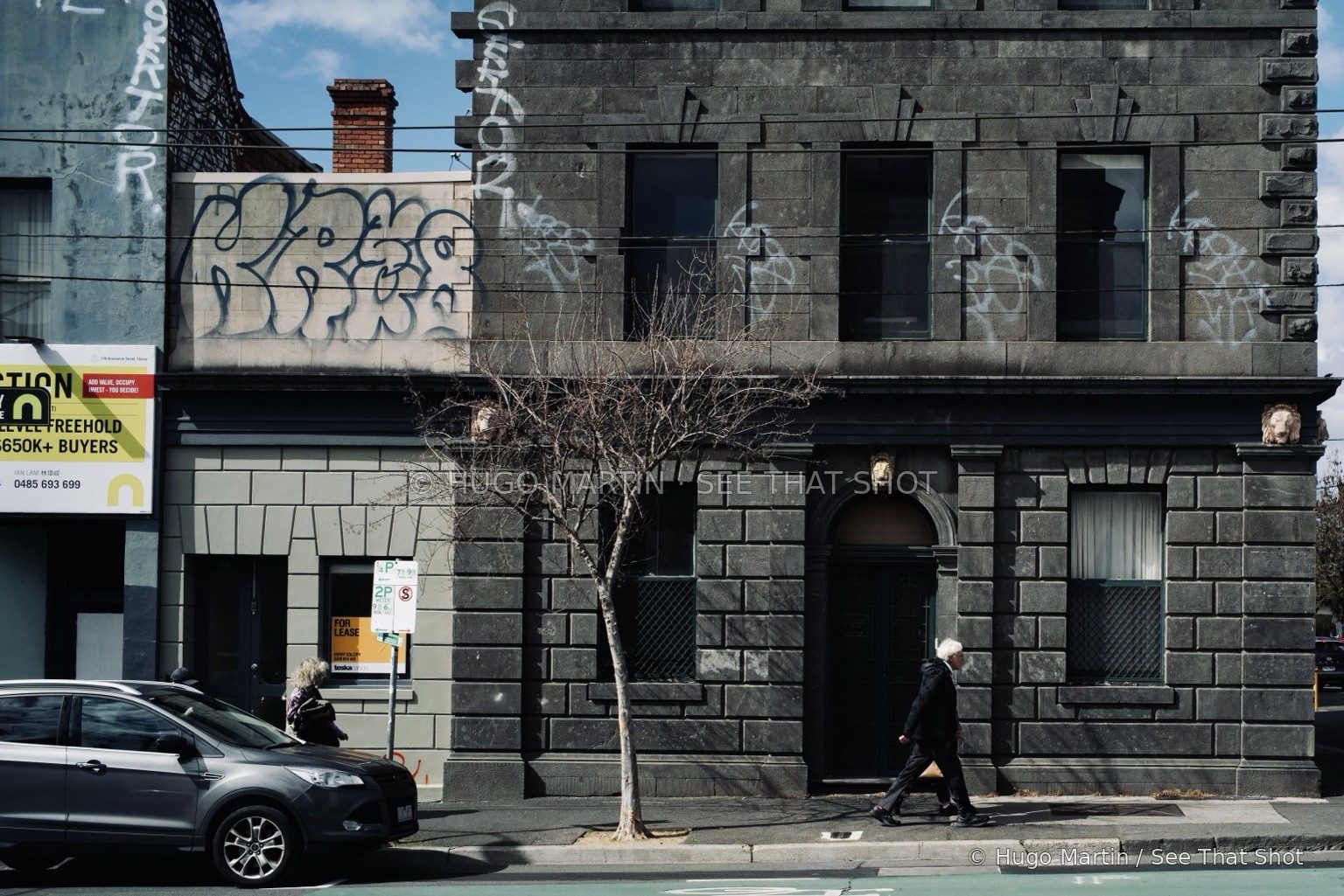 A pedestrian and a parked car in front of a weathered stone building