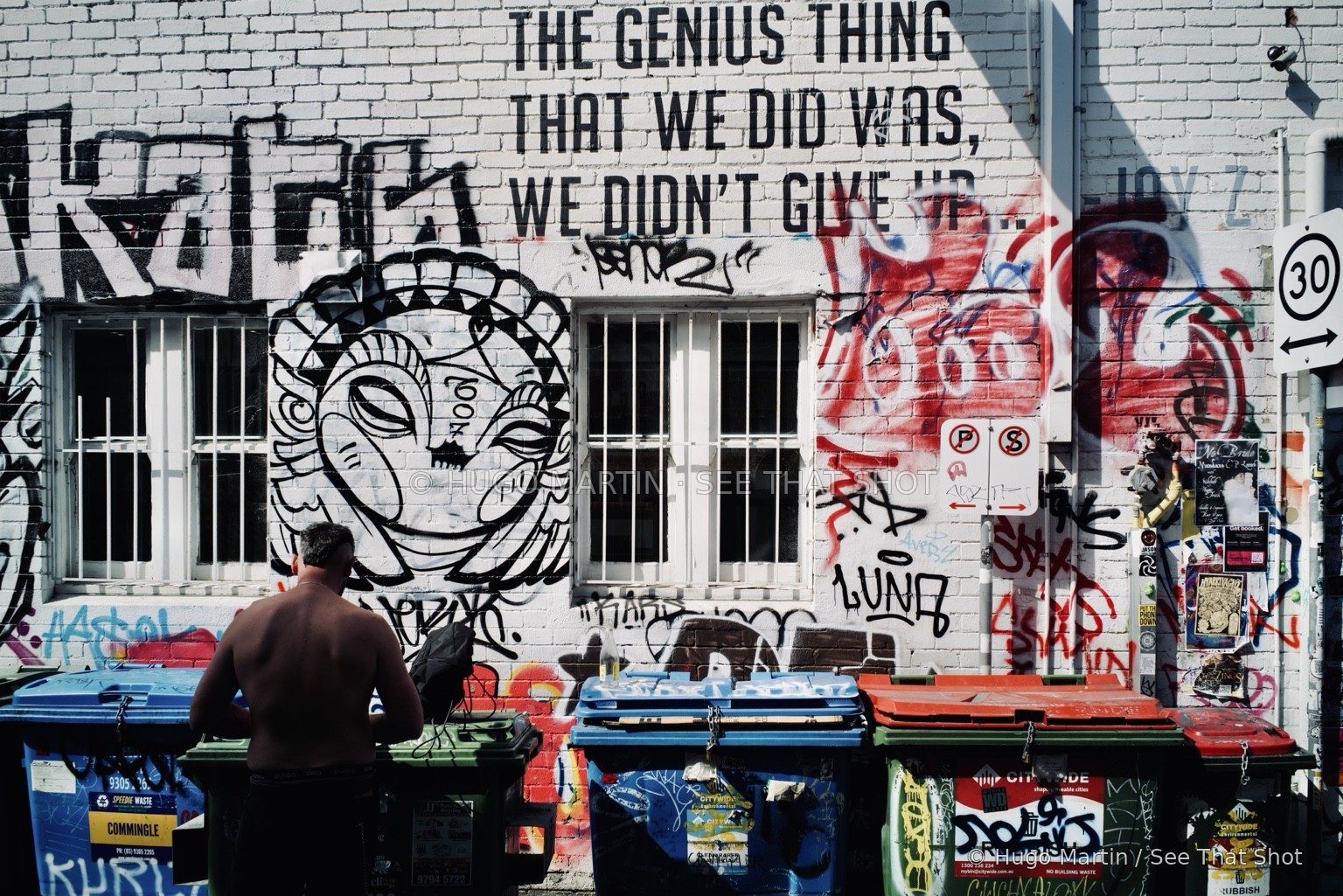 A passerby beside a wall covered in graffiti and illustrated faces